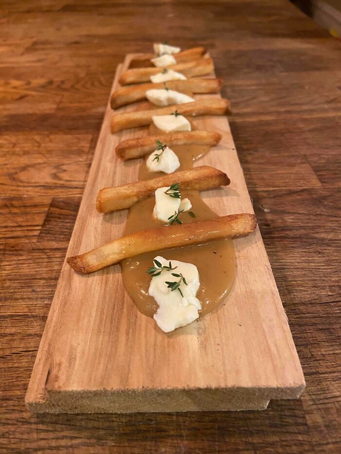 French fries with gravy and cream on a wooden board, an example of dishes that are just stupid in presentation.