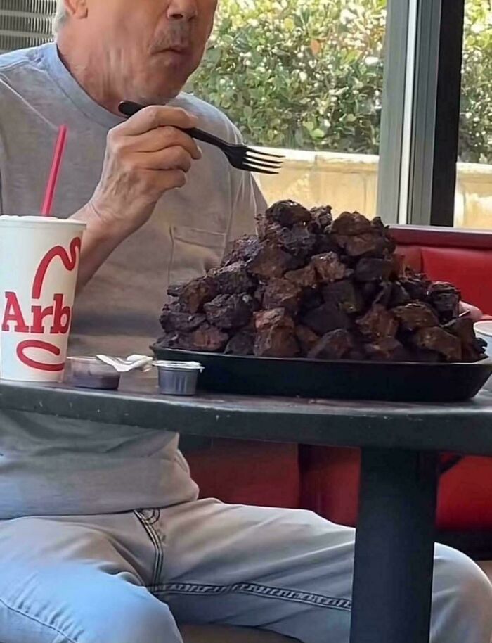 Man eating an enormous pile of burnt food at a fast food restaurant, showcasing one of the most stupid dishes.