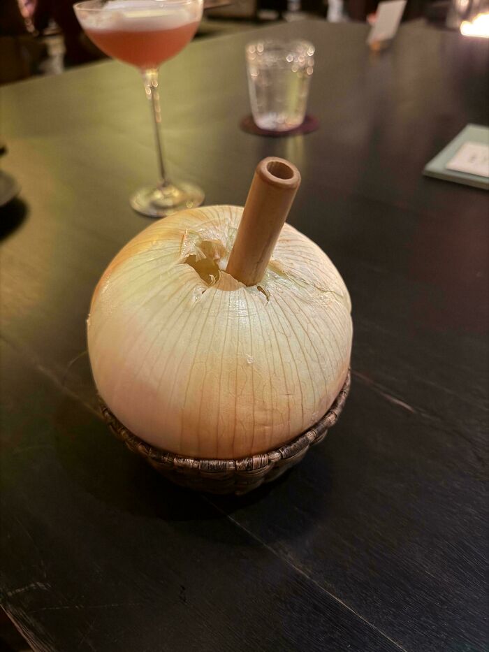 A large raw onion used as a drink container with a straw, demonstrating one of the dishes that are just stupid.