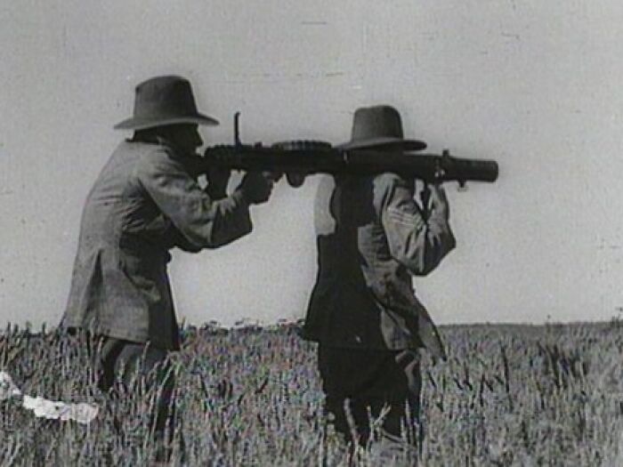 Two men in hats aiming a vintage rocket launcher in a field, depicting a hilarious historical event.