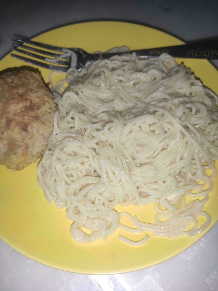 Plain white noodles and a dry meat patty served on a yellow plate showing a simple dish from the stupid dishes collection.