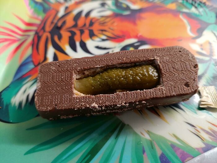 Chocolate bar with a pickle in the center placed on a colorful tiger-themed plate featuring unusual dishes.