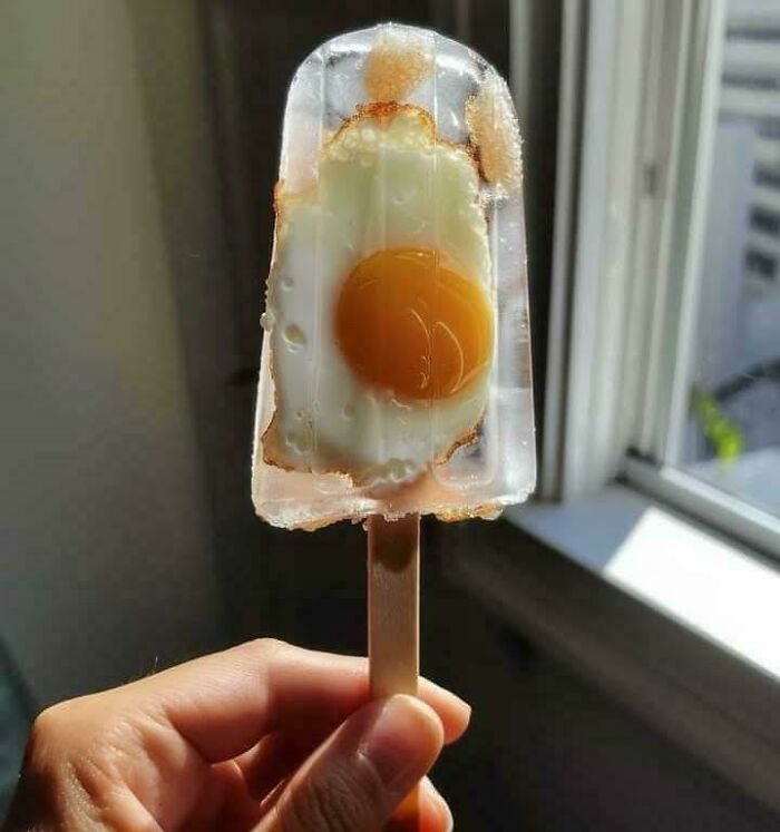 Fried egg frozen inside a clear popsicle held by hand near a window showcasing bizarre dishes from stupid food creations.