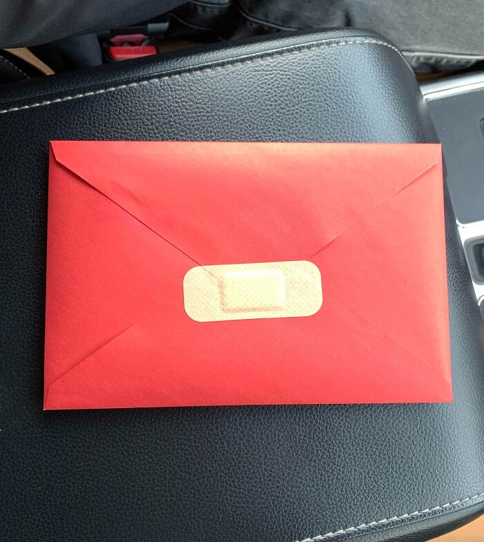 Red envelope sealed with a bandage on black leather surface, showcasing unhinged pics of people doing exactly what they were asked to do.