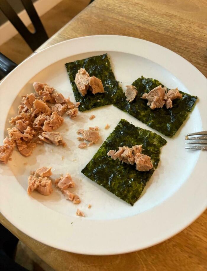 Three seaweed sheets topped with small chunks of tuna on a white plate, showing a simple and unusual dish idea.