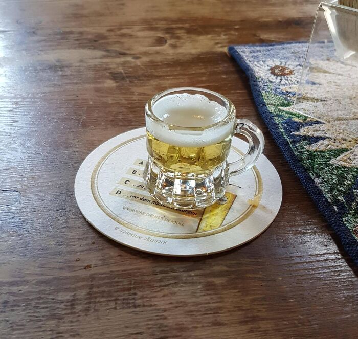 Miniature beer mug filled with beer placed on a coaster on a wooden table in unhinged pics of people doing exactly what asked