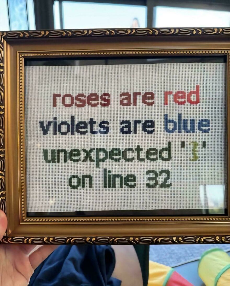 Framed cross-stitch with a humorous programming meme about an unexpected character error on line 32, highlighting debugging.
