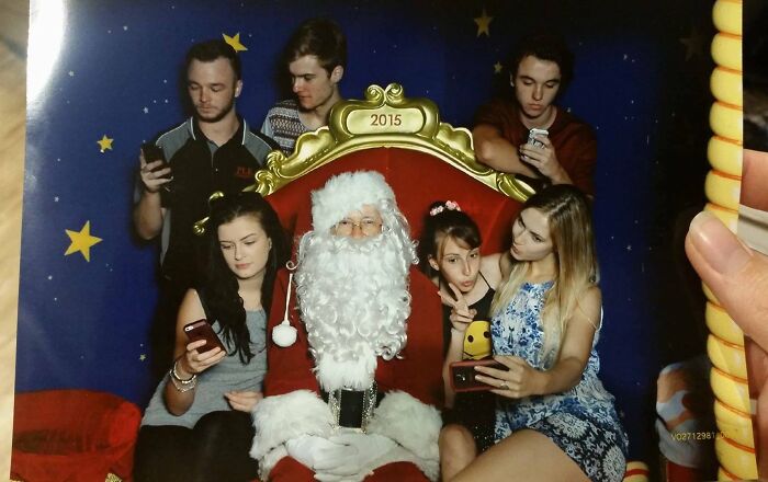 Group of young people sitting with Santa Claus, all distracted by their phones in a petty revenge themed setting.