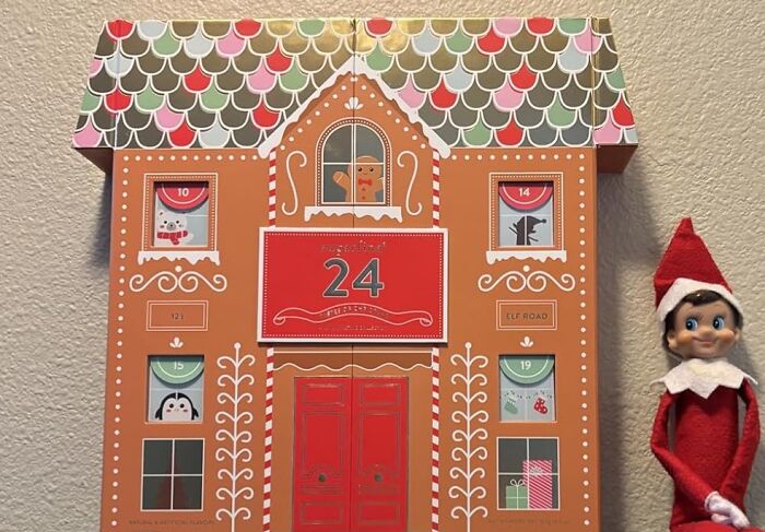 Gingerbread house style advent calendar with numbered doors and a festive elf doll beside it for Christmas countdown.