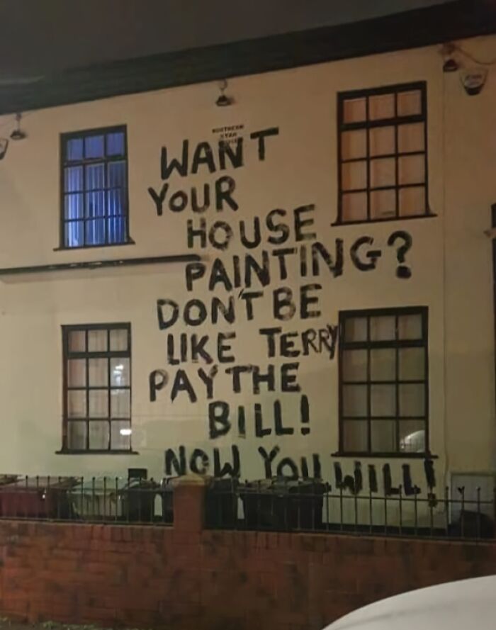 Graffiti on a house wall showing petty revenge message about paying a painting bill, highlighting consequences of being a jerk.