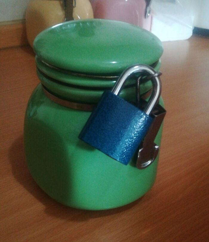 Green jar locked with a blue padlock on a wooden table, illustrating petty revenge and not being a jerk to others.