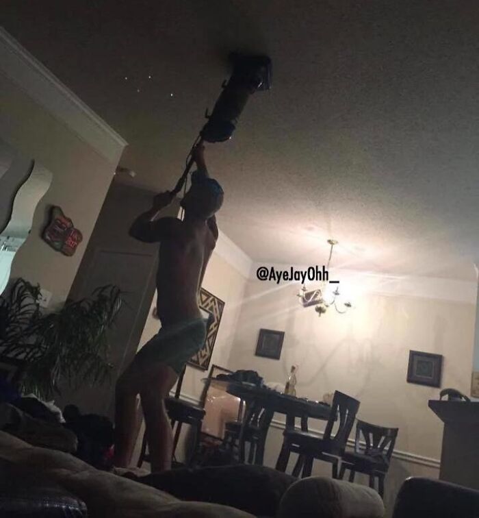 Man using a vacuum on the ceiling in a dimly lit room, an example of petty revenge action indoors.