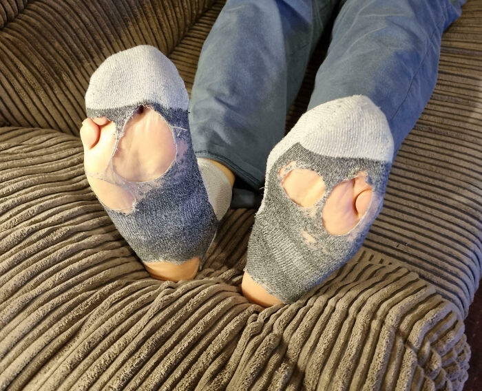 Worn-out socks with large holes on feet resting on a couch, illustrating family frustrations shared online.