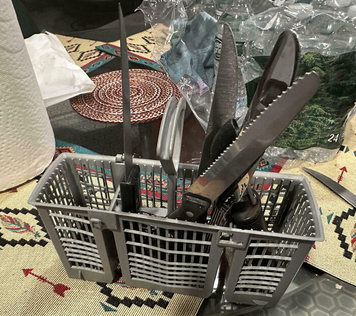 Cutlery and sharp knives placed haphazardly in a dishwasher basket, illustrating family frustration moments shared online.