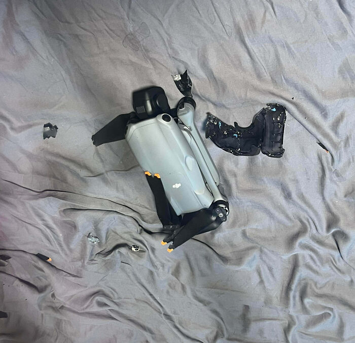Broken drone parts scattered on a wrinkled gray bedsheet, showing damage likely caused by a family member's actions.