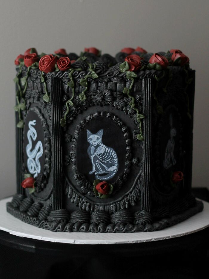 Dark gothic cake with skeleton cat and snake designs, decorated with red frosting roses, showcasing gorgeous baked goods artistry.