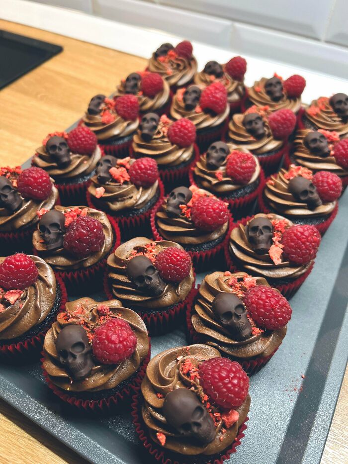 Chocolate cupcakes with raspberries and edible skull decorations, showcasing gorgeous baked goods with creative kitchen artistry.