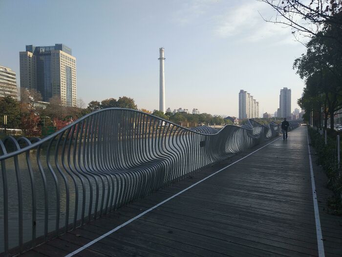 Modern curved metal railing along wooden walkway by river in city, showcasing smart ideas and inventions solving problems.