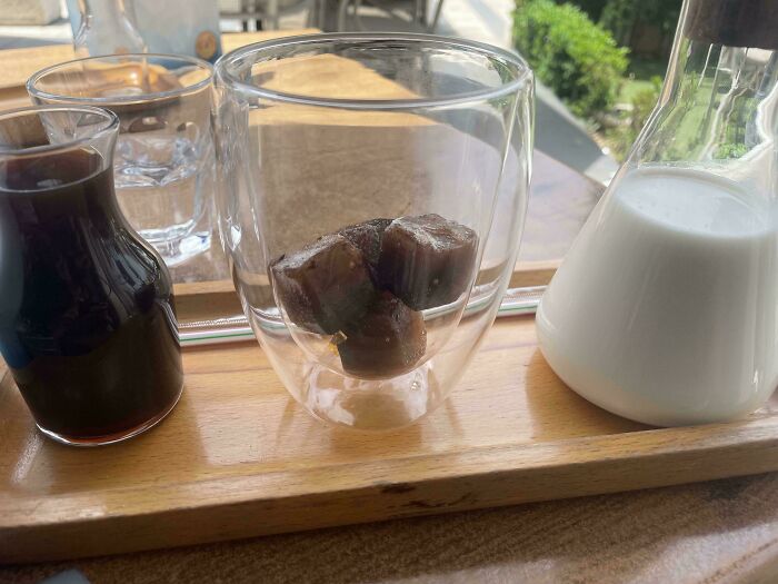 Glass with coffee ice cubes between small glass containers of coffee and milk on a wooden tray, smart idea to keep drinks cold.