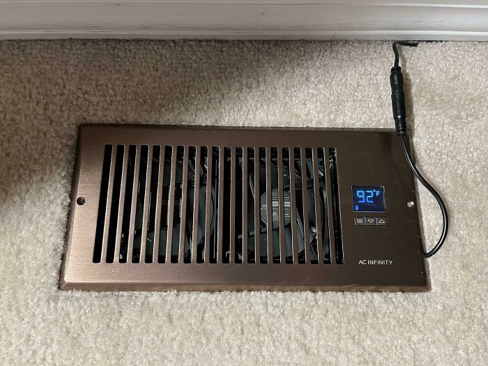 Vent cover with built-in fan and digital temperature display installed on carpeted floor, showcasing smart invention solving heating problems.