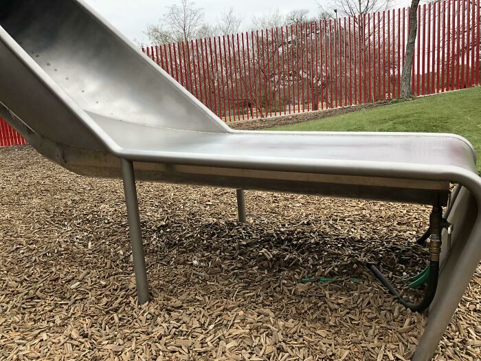 Metal playground slide with water pipe attachment underneath, showcasing smart invention that solves water drainage problems outdoors.