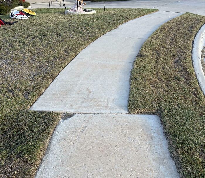 Sidewalk with a poorly aligned concrete slab and uneven grass edges, illustrating people not even trying.