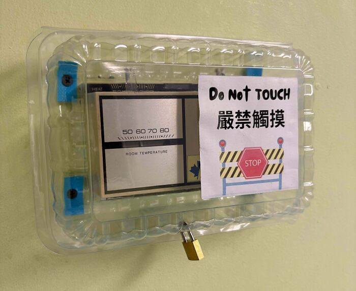 Thermostat covered in plastic with a Do Not Touch sign and padlock, a funny example of people not even trying.