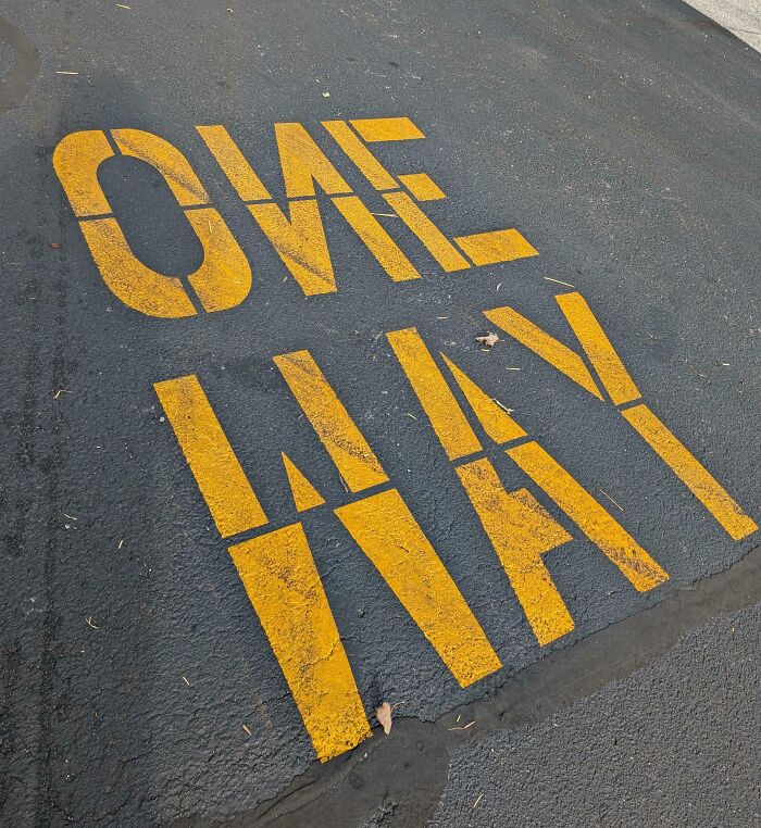 Yellow parking lot lines misspelled as ONE WAY, illustrating a funny example of people not even trying at the job.