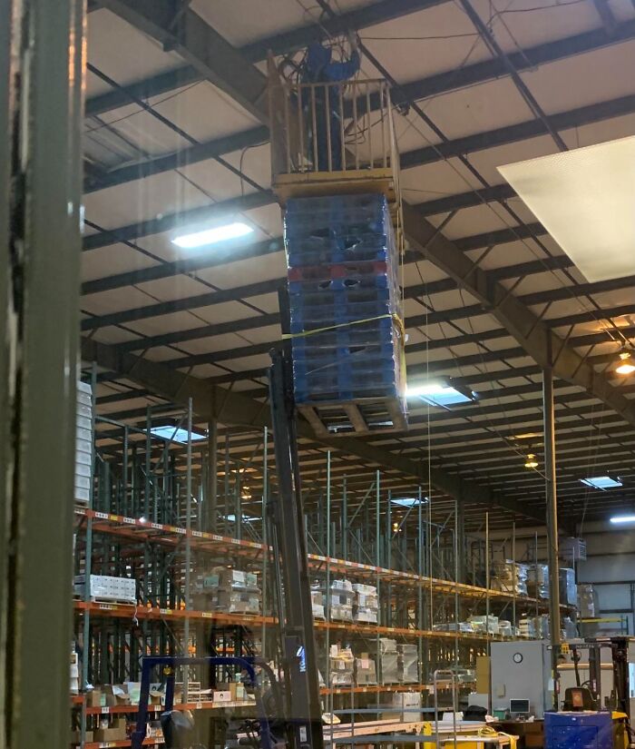 Forklift lifting pallets incorrectly with a person on top in a warehouse showing people not even trying at work.