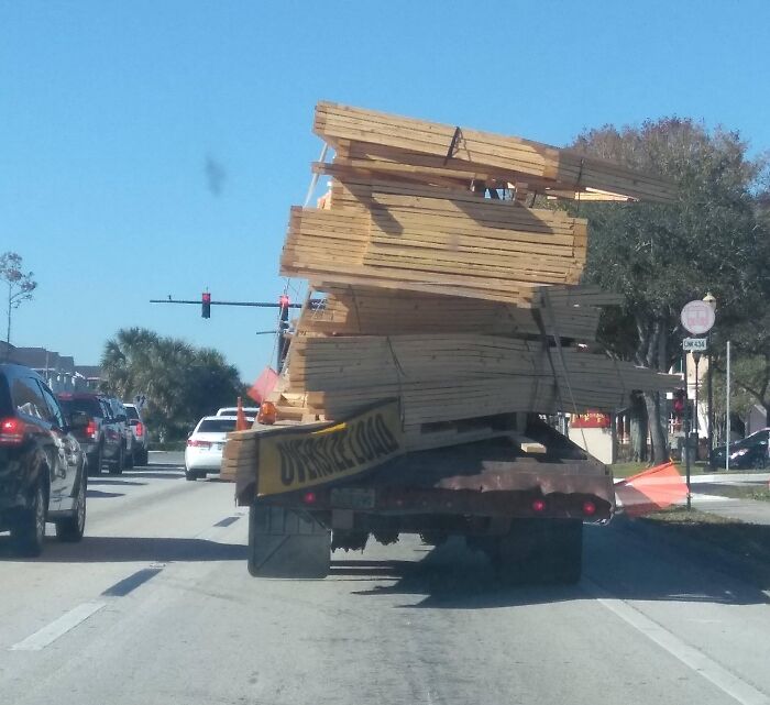 Truck overloaded with lumber leaning dangerously, illustrating funny examples of people not even trying on the job.