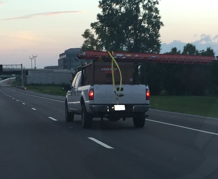 Pickup truck on highway with a ladder improperly secured, illustrating funny examples of people not even trying at work.