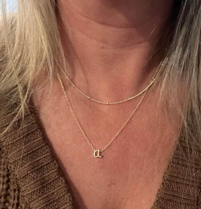 Close-up of a person wearing delicate gold necklaces, showcasing a cozy burr basket style with a knit brown sweater.