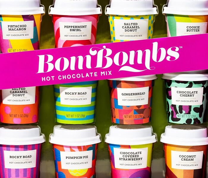 Assorted colorful BonBombs hot chocolate mix cups arranged as a cozy burr basket goodies starter kit.