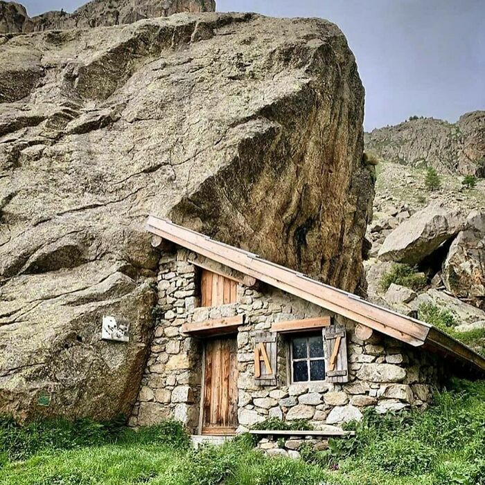 Stone off-grid cabin built into a rocky hillside surrounded by greenery, perfect for a cozy mountain retreat.