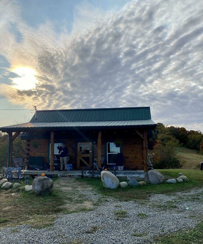 Cozy off-grid cabin with green metal roof set in a natural landscape under a cloudy sunset sky.