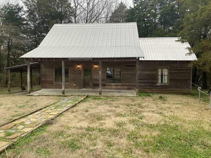 Rustic cozy off-grid cabin with metal roof surrounded by trees, inviting peaceful disconnection in a natural setting.