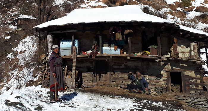 Rustic off-grid cabin in snowy mountainous area with people outside, showcasing cozy and remote living.