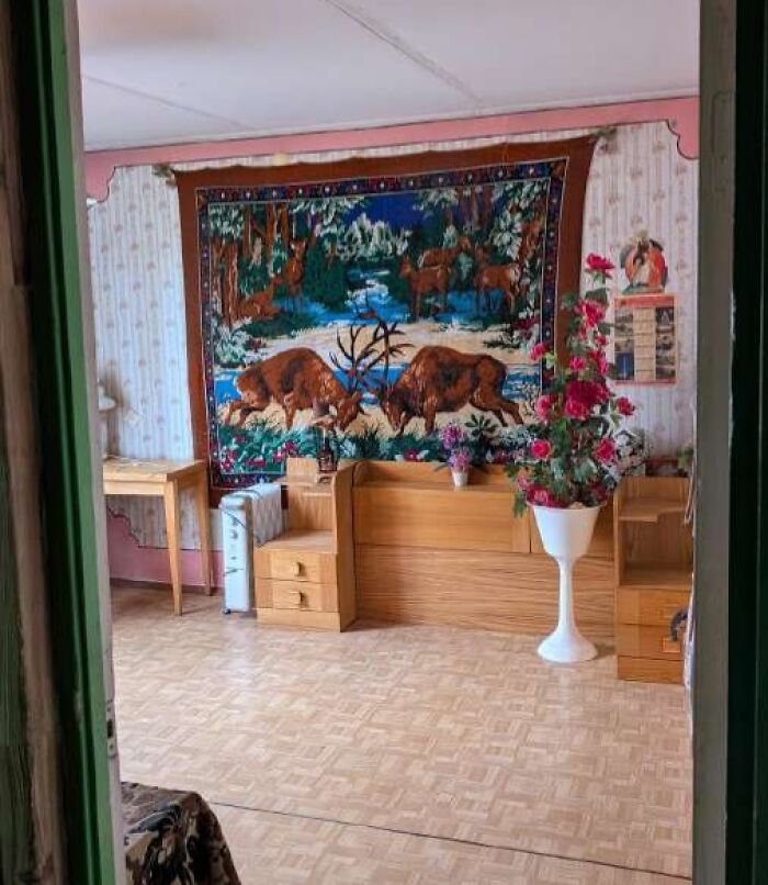 Sala con decoración retro, tapiz con ciervos, muebles de madera y planta con flores rosas en maceta blanca, listado inmobiliario entretenido.