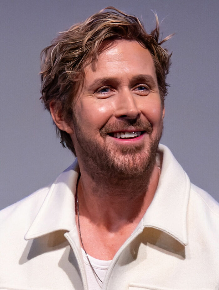 Ryan Gosling smiling with casual light jacket and necklace, highlighting his bio and career in entertainment.