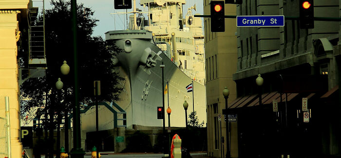 Massive ship docked at a city street intersection with traffic lights and buildings, showing world from a different perspective.