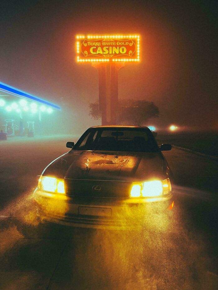 Classic car with headlights on in foggy night near a glowing casino sign, showcasing our world from a different perspective.