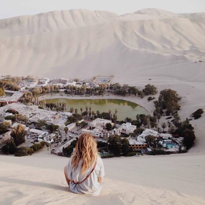 Person sitting on sand dune overlooking an oasis village, one of the amazing pics showing our world from a different perspective