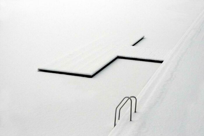Minimalistic snowy scene showing a frozen pool and walkway, capturing an amazing perspective of our world in winter.