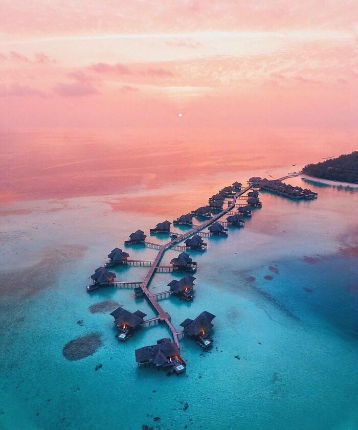 Aerial view of overwater bungalows on turquoise water at sunset, showcasing amazing pics of the world from a different perspective.