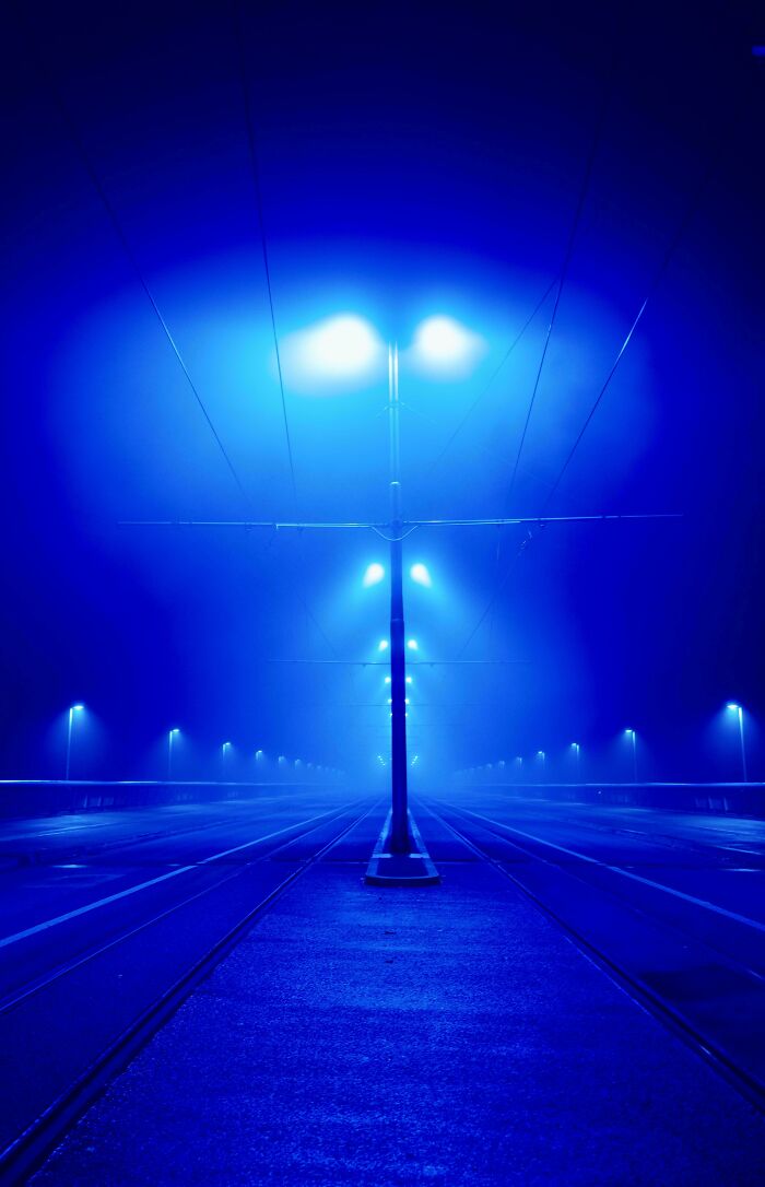Empty tram tracks and illuminated streetlights in dense blue fog, showing our world from a different perspective.