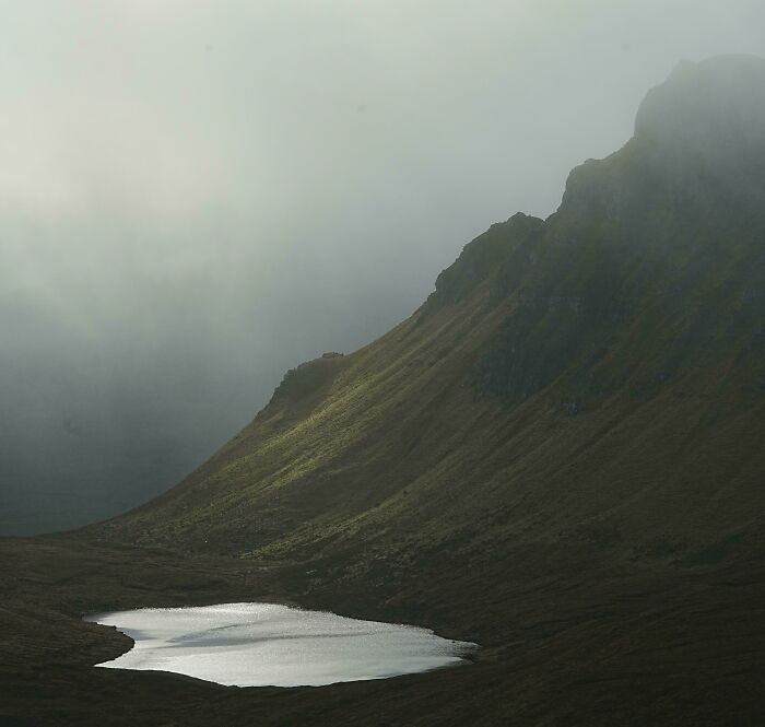 Foggy mountain slope with a reflective lake below, showcasing an amazing perspective of our world’s natural beauty.