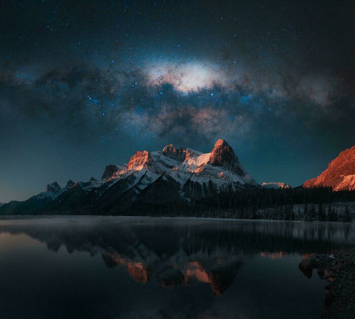Snow-covered mountain peaks illuminated by a starry night sky, reflected in a calm lake showcasing amazing pics perspective.
