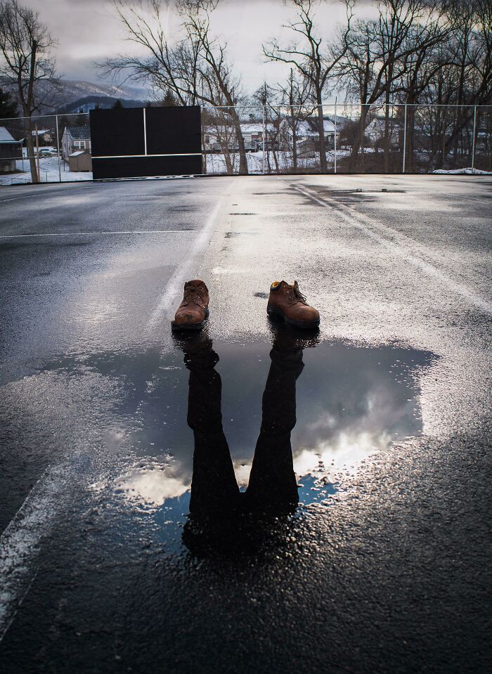 Pair of boots on wet pavement with reflection creating illusion of legs, an amazing pic showing our world from a different perspective