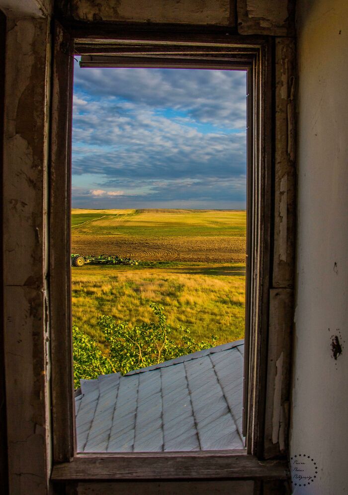 View of expansive fields and partly cloudy sky through an old window, showing our world from a different perspective.