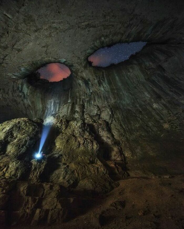 Person exploring cave with flashlight under starry sky through natural rock formations, showing our world perspective.